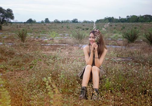 A beautiful woman with long hair in a dress sitting on a meadow and flowers in the evening light.
