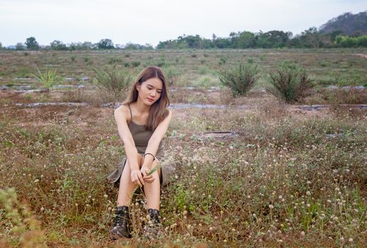 A beautiful woman with long hair in a dress sitting on a meadow and flowers in the evening light.