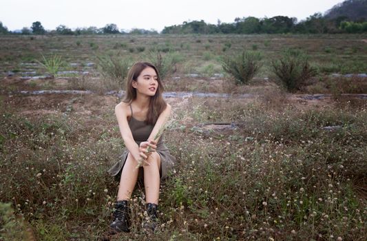 A beautiful woman with long hair in a dress sitting on a meadow and flowers in the evening light.