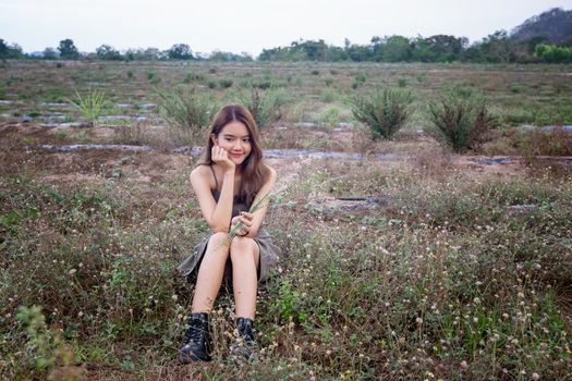 A beautiful woman with long hair in a dress sitting on a meadow and flowers in the evening light.