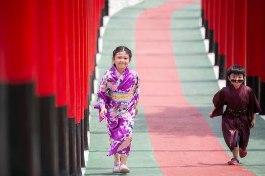 Two kids in kimono walking into at the shrine red gate, in Japanese garden.