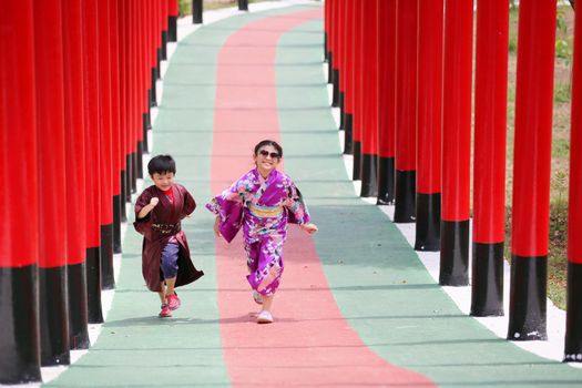 Two kids in kimono walking into at the shrine red gate, in Japanese garden.