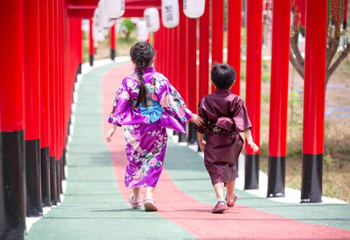 Two kids in kimono walking into at the shrine red gate, in Japanese garden.