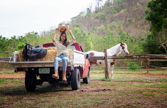 A woman in a cowgirl style sits in a horse ranch with a western farm environment.