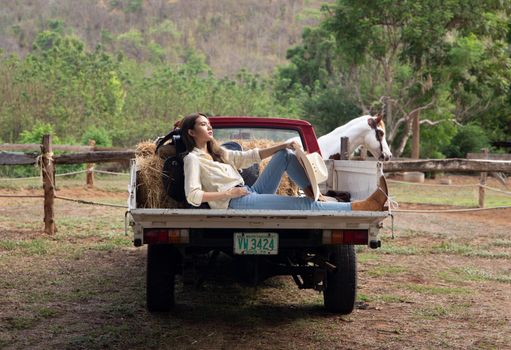 A woman in a cowgirl style sits in a horse ranch with a western farm environment.