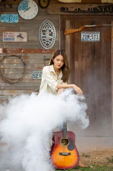 A woman in a cowgirl style sits in a horse ranch with a western farm environment.