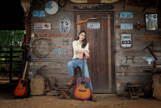 A woman in a cowgirl style sits in a horse ranch with a western farm environment.