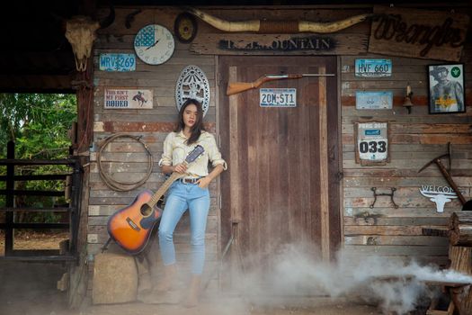 A woman in a cowgirl style sits in a horse ranch with a western farm environment.