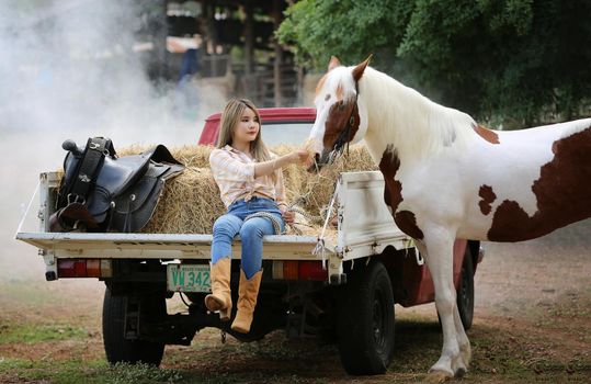 A woman in a cowgirl style sits in a horse ranch with a western farm environment.