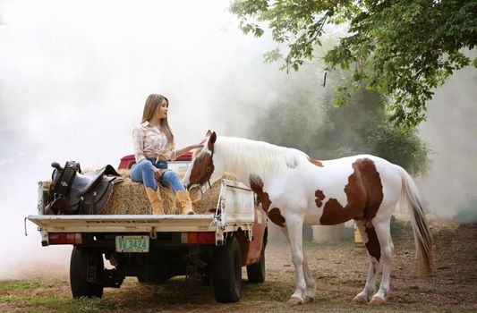 A woman in a cowgirl style sits in a horse ranch with a western farm environment.