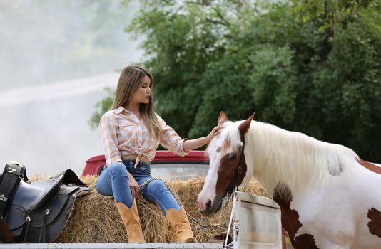 A woman in a cowgirl style sits in a horse ranch with a western farm environment.