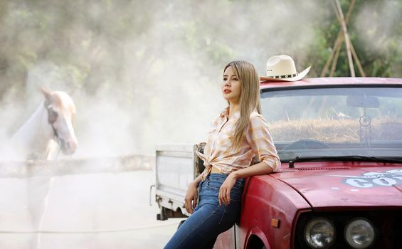 A woman in a cowgirl style sits in a horse ranch with a western farm environment.