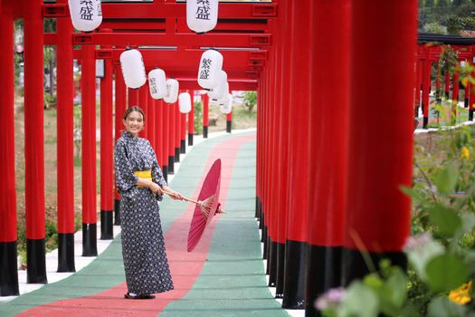 woman in kimono holding umbrella walking into at the shrine red gate, in Japanese garden.