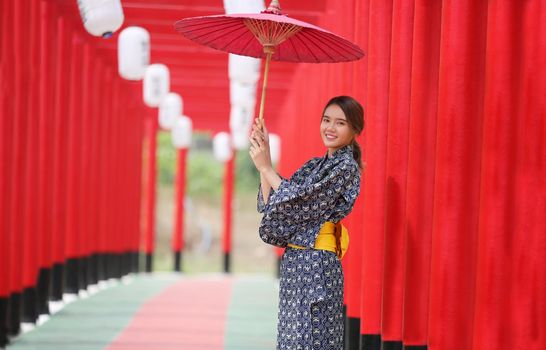 woman in kimono holding umbrella walking into at the shrine red gate, in Japanese garden.