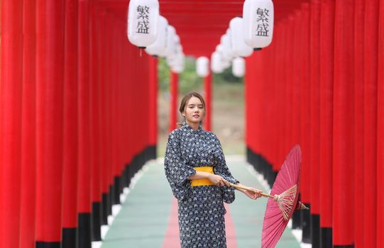 woman in kimono holding umbrella walking into at the shrine red gate, in Japanese garden.