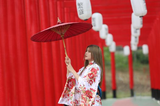 woman in kimono holding umbrella walking into at the shrine red gate, in Japanese garden.