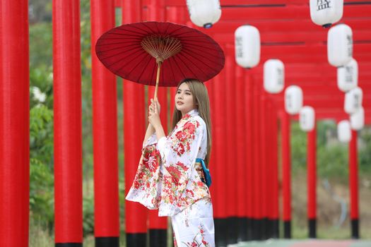 woman in kimono holding umbrella walking into at the shrine red gate, in Japanese garden.