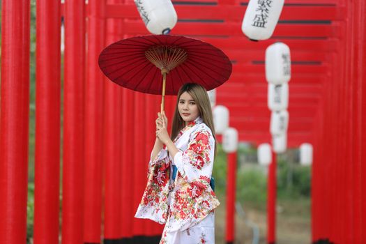 woman in kimono holding umbrella walking into at the shrine red gate, in Japanese garden.