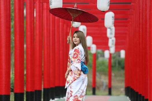 woman in kimono holding umbrella walking into at the shrine red gate, in Japanese garden.
