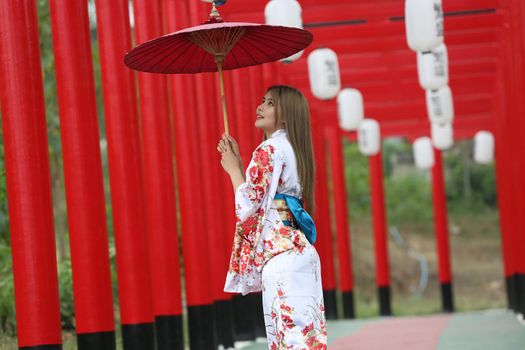 woman in kimono holding umbrella walking into at the shrine red gate, in Japanese garden.