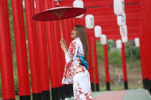 woman in kimono holding umbrella walking into at the shrine red gate, in Japanese garden.