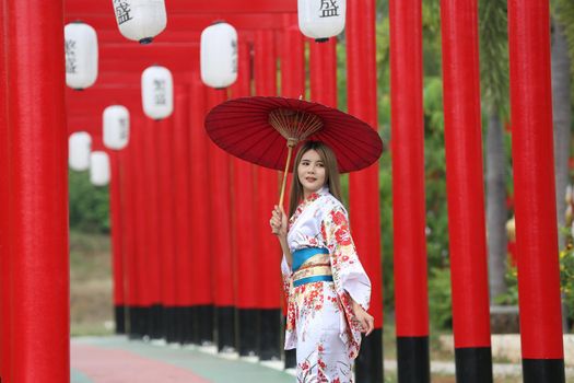 woman in kimono holding umbrella walking into at the shrine red gate, in Japanese garden.