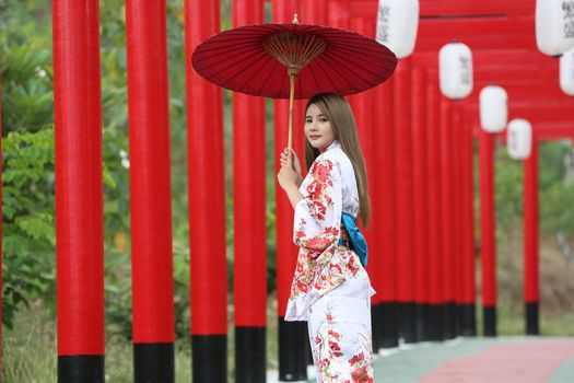 woman in kimono holding umbrella walking into at the shrine red gate, in Japanese garden.