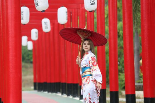woman in kimono holding umbrella walking into at the shrine red gate, in Japanese garden.