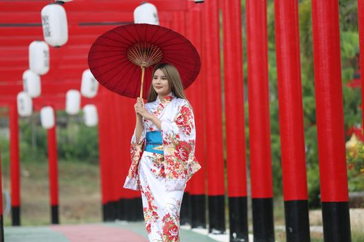 woman in kimono holding umbrella walking into at the shrine red gate, in Japanese garden.