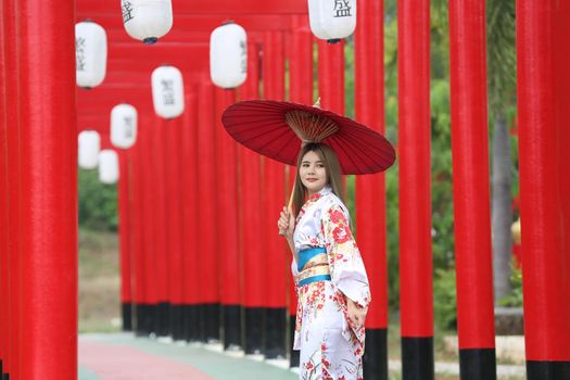 woman in kimono holding umbrella walking into at the shrine red gate, in Japanese garden.