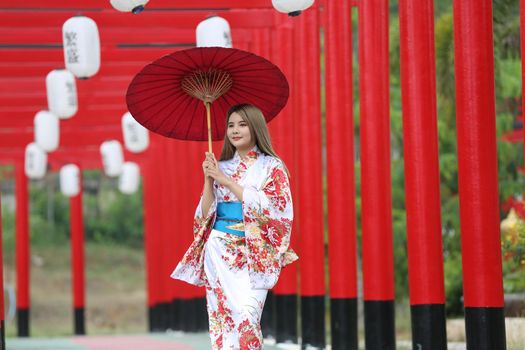 woman in kimono holding umbrella walking into at the shrine red gate, in Japanese garden.