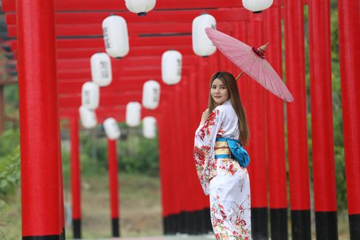 woman in kimono holding umbrella walking into at the shrine red gate, in Japanese garden.