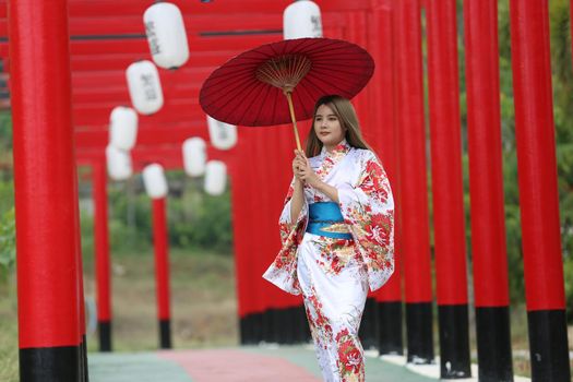 woman in kimono holding umbrella walking into at the shrine red gate, in Japanese garden.