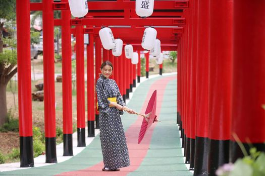 woman in kimono holding umbrella walking into at the shrine red gate, in Japanese garden.