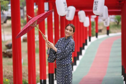 woman in kimono holding umbrella walking into at the shrine red gate, in Japanese garden.