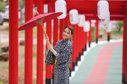 woman in kimono holding umbrella walking into at the shrine red gate, in Japanese garden.