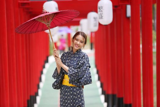 woman in kimono holding umbrella walking into at the shrine red gate, in Japanese garden.