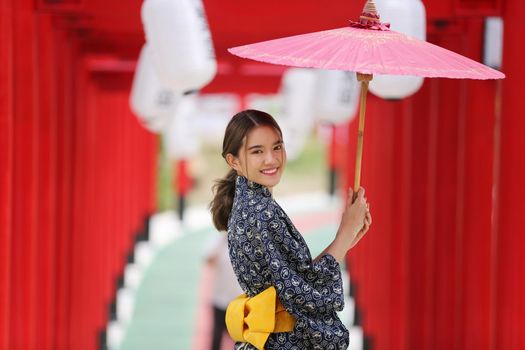 woman in kimono holding umbrella walking into at the shrine red gate, in Japanese garden.