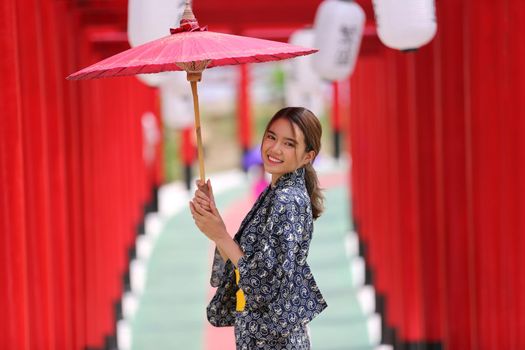 woman in kimono holding umbrella walking into at the shrine red gate, in Japanese garden.