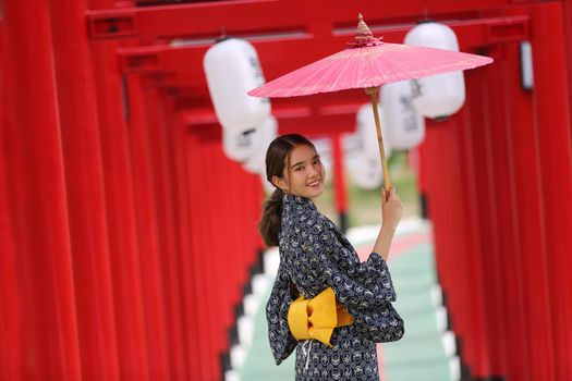 woman in kimono holding umbrella walking into at the shrine red gate, in Japanese garden.