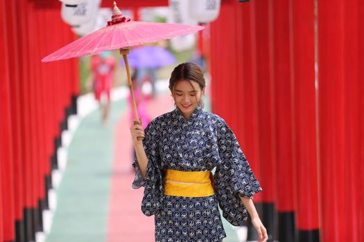woman in kimono holding umbrella walking into at the shrine red gate, in Japanese garden.
