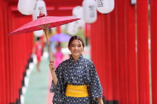 woman in kimono holding umbrella walking into at the shrine red gate, in Japanese garden.
