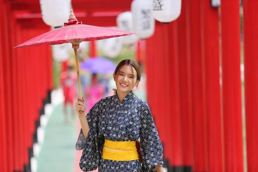 woman in kimono holding umbrella walking into at the shrine red gate, in Japanese garden.