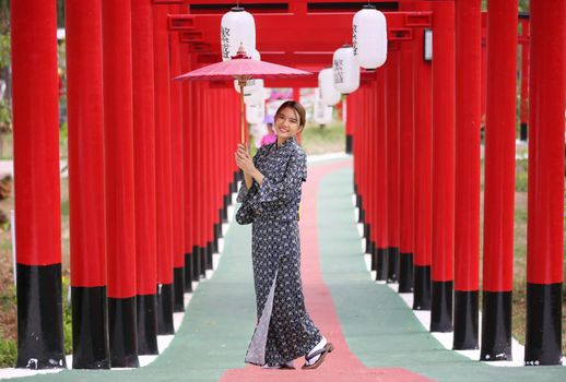 woman in kimono holding umbrella walking into at the shrine red gate, in Japanese garden.