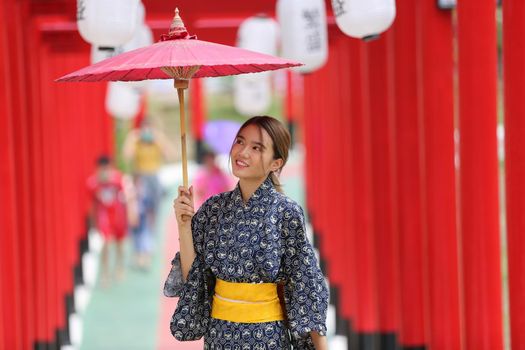 woman in kimono holding umbrella walking into at the shrine red gate, in Japanese garden.