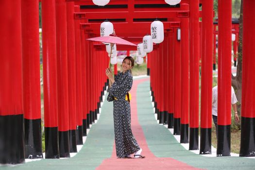 woman in kimono holding umbrella walking into at the shrine red gate, in Japanese garden.