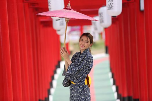 woman in kimono holding umbrella walking into at the shrine red gate, in Japanese garden.