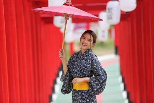 woman in kimono holding umbrella walking into at the shrine red gate, in Japanese garden.