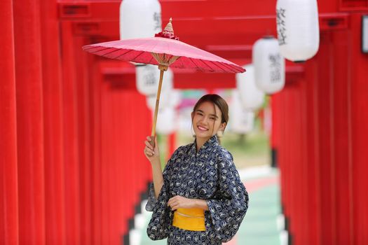 woman in kimono holding umbrella walking into at the shrine red gate, in Japanese garden.