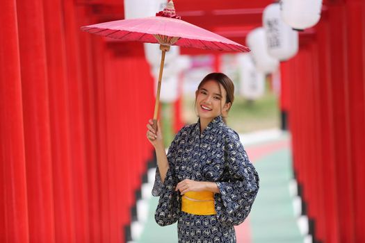 woman in kimono holding umbrella walking into at the shrine red gate, in Japanese garden.